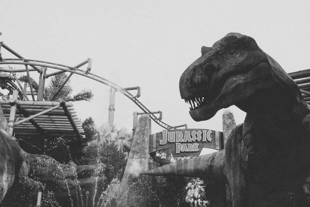 A black and white photo of the iconic “Jurassic Park” sign at the dinosaur theme park, with a T-rex in the background. Shot on Kodak film in the style of Steven Spielberg. –ar 128:85