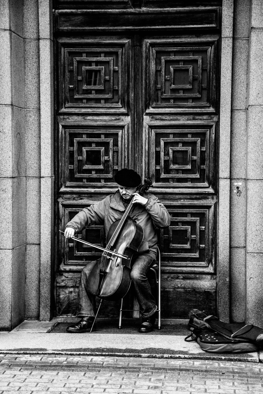 A street musician playing the cello in front of an ornate wooden door, black and white photography, street style, in the style of Nikon D850. –ar 85:128