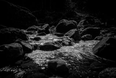 Black and white photography of water flowing between rocks in the forest, nature, contrast, dark tones, shadows, rocks, stream, nature photography, in the style of Leica Q2 --ar 128:85