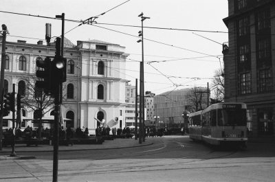 Berlin street, buildings and people in the background, a white tram passing in the style of Kodak Trix, black and white photo, grainy film effect. --ar 32:21