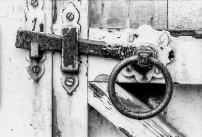 Close up of an old white wooden door with a metal ring knocker. Black and white photography in the style of Leica M6 and Ilford. --ar 128:87