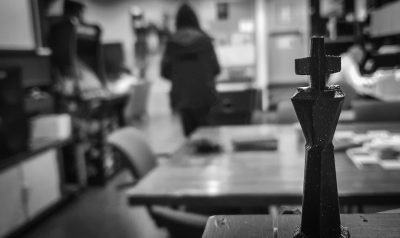 Black and white photography of an iron chess piece in the foreground, blurry high school classroom with students working on their homework in background. --ar 32:19