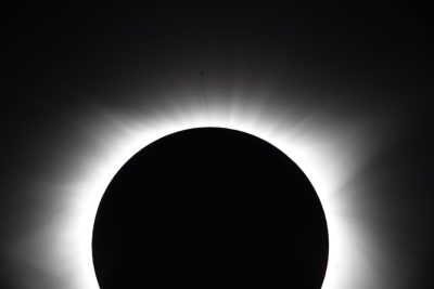 The silhouette of the total solar eclipse seen from Tokyo, Japan. The black sun is centered in the frame against a white background. It is framed by a dark sky with soft light rays emanating from behind it. A silhouette effect adds depth to the scene. --ar 128:85