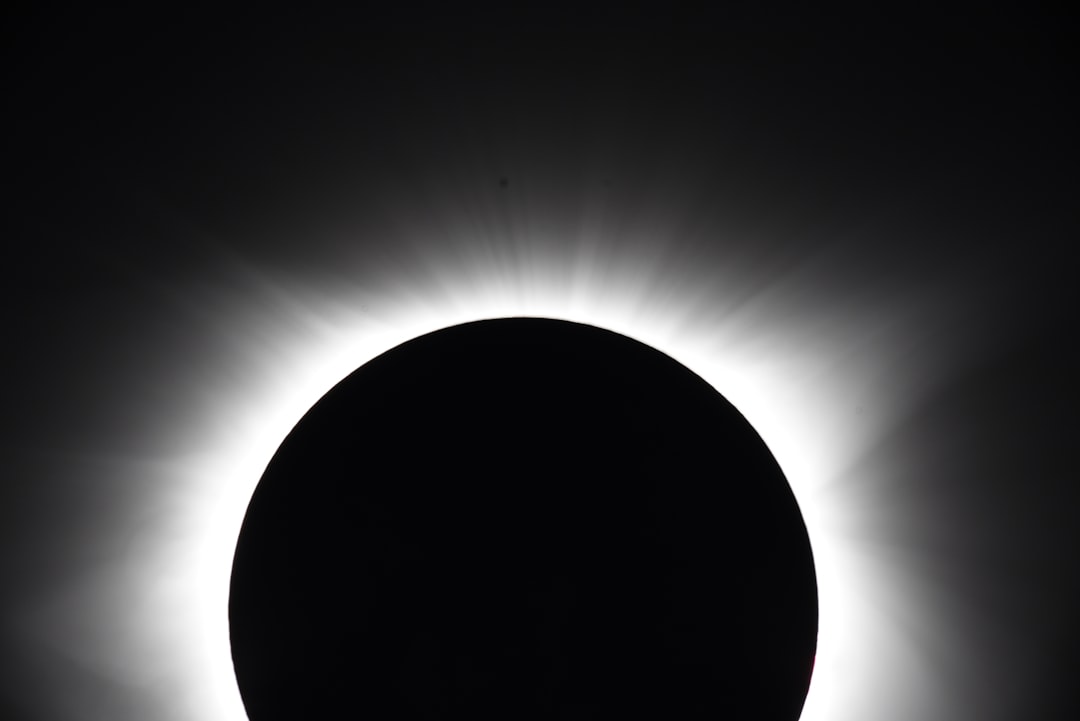 The silhouette of the total solar eclipse seen from Tokyo, Japan. The black sun is centered in the frame against a white background. It is framed by a dark sky with soft light rays emanating from behind it. A silhouette effect adds depth to the scene. –ar 128:85