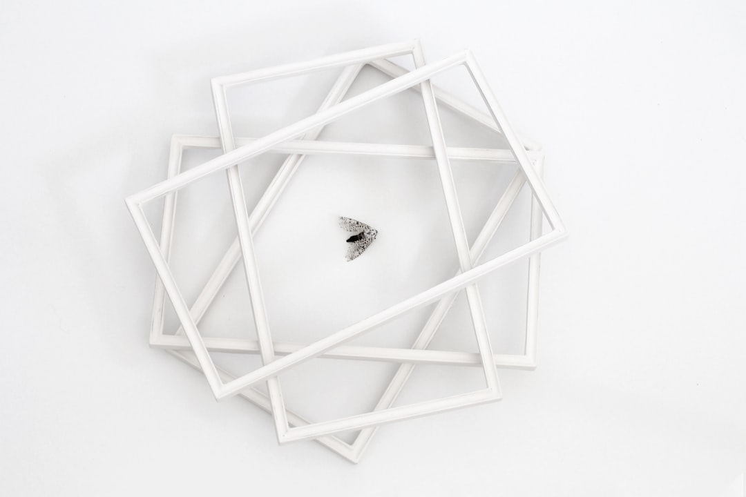 A geometric white sculpture with three-dimensional frames on the wall, surrounded in the style of a diamond ring in an empty space, white background, overhead view, product photography, studio lighting, minimalism, modern art style, simple and clean design. –ar 128:85