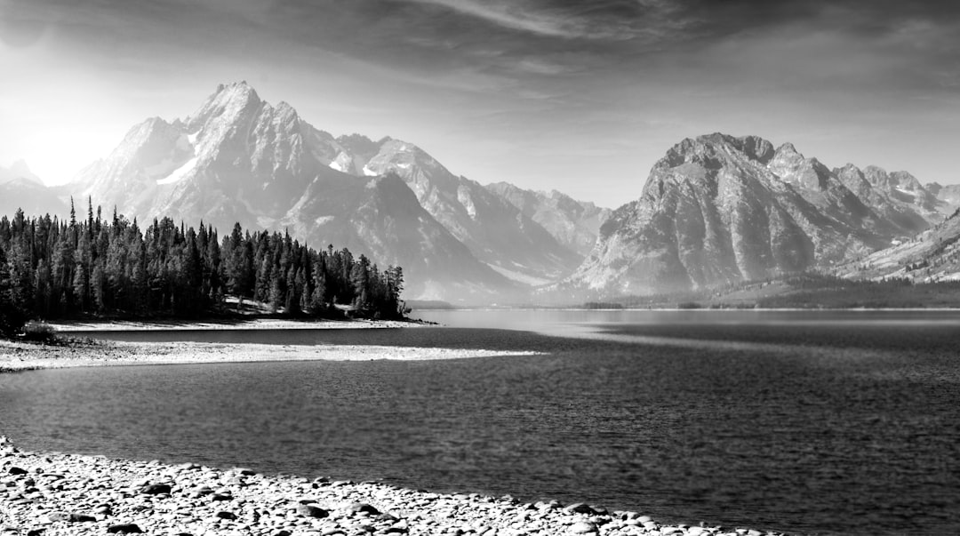 Black and white photo of the Grand Teton National Park with sharp mountains, trees on the shore, lake water, sky, high resolution, high detail, hyper realistic, award winning photography, in the style of HDR. –ar 128:71