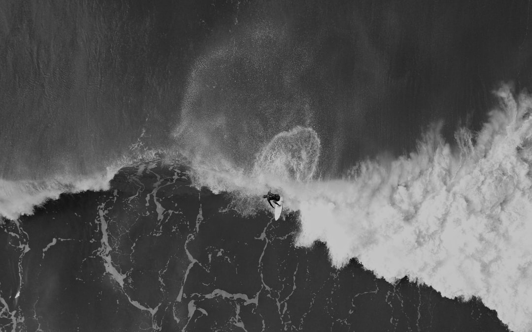 Black and white drone photo of surfer riding wave, aerial view, black ocean water, huge waves –ar 8:5