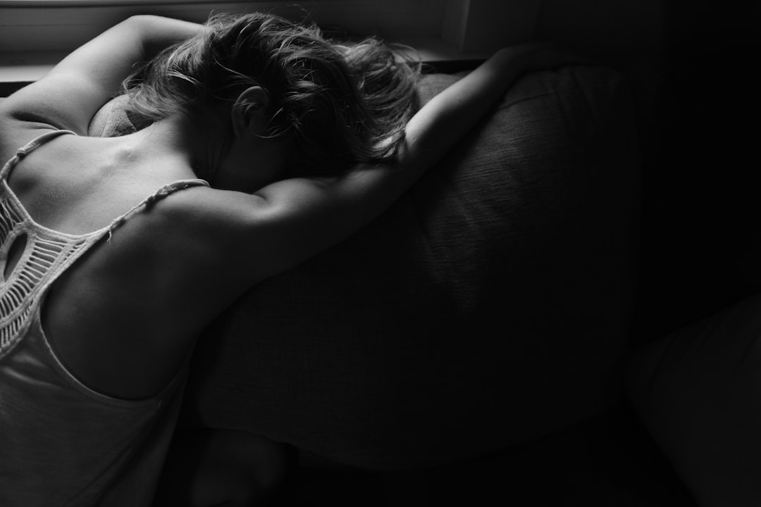 A woman is lying on the sofa, head down and crying with her hands behind his back. The photo was taken from above in black and white, creating a dark atmosphere. Her hair had been curled up to emphasize details of facial expression. She’s wearing a tank top that shines slightly under the light. There should be some soft shadows cast by sunlight through the window. It captures an moment where she feels lonely or depressed due to inner pain. Shot at f/2.8, –ar 128:85