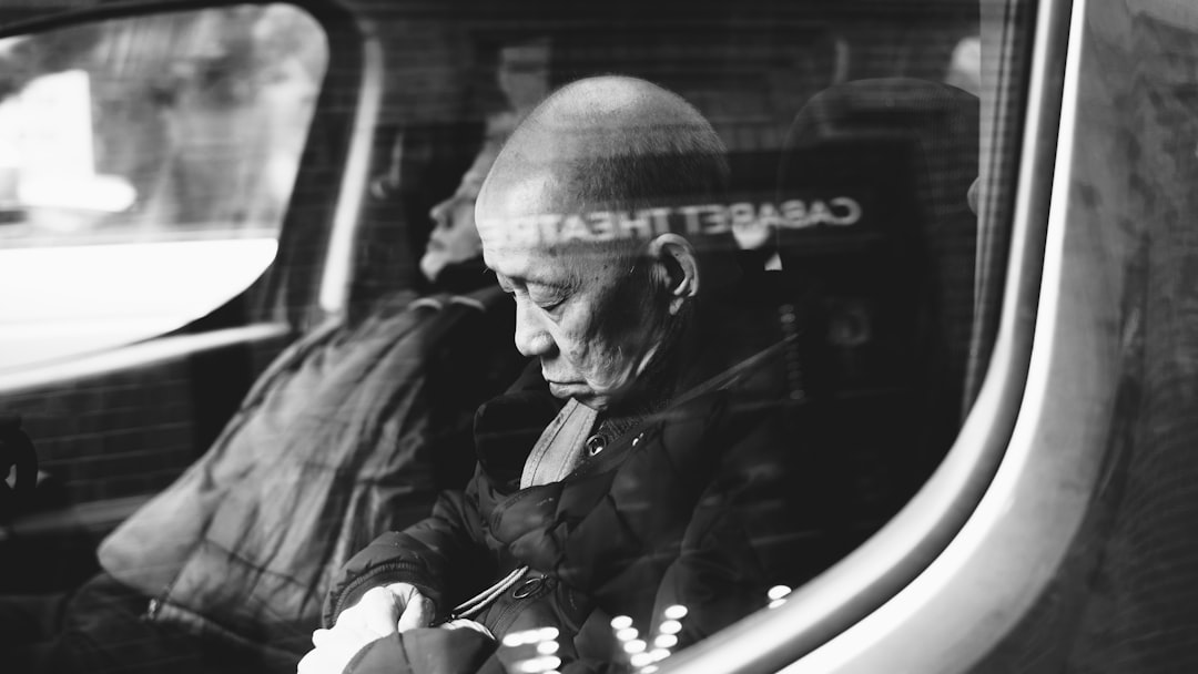 Black and white street photography of an old Asian man sitting in the back seat inside a London taxi. He is wearing gloves and has no hair on his head, looking out through the window with a pensive expression. Shot in the style of [Richard Kern](https://goo.gl/search?artist%20Richard%20Kern), with dark contrast. –ar 16:9