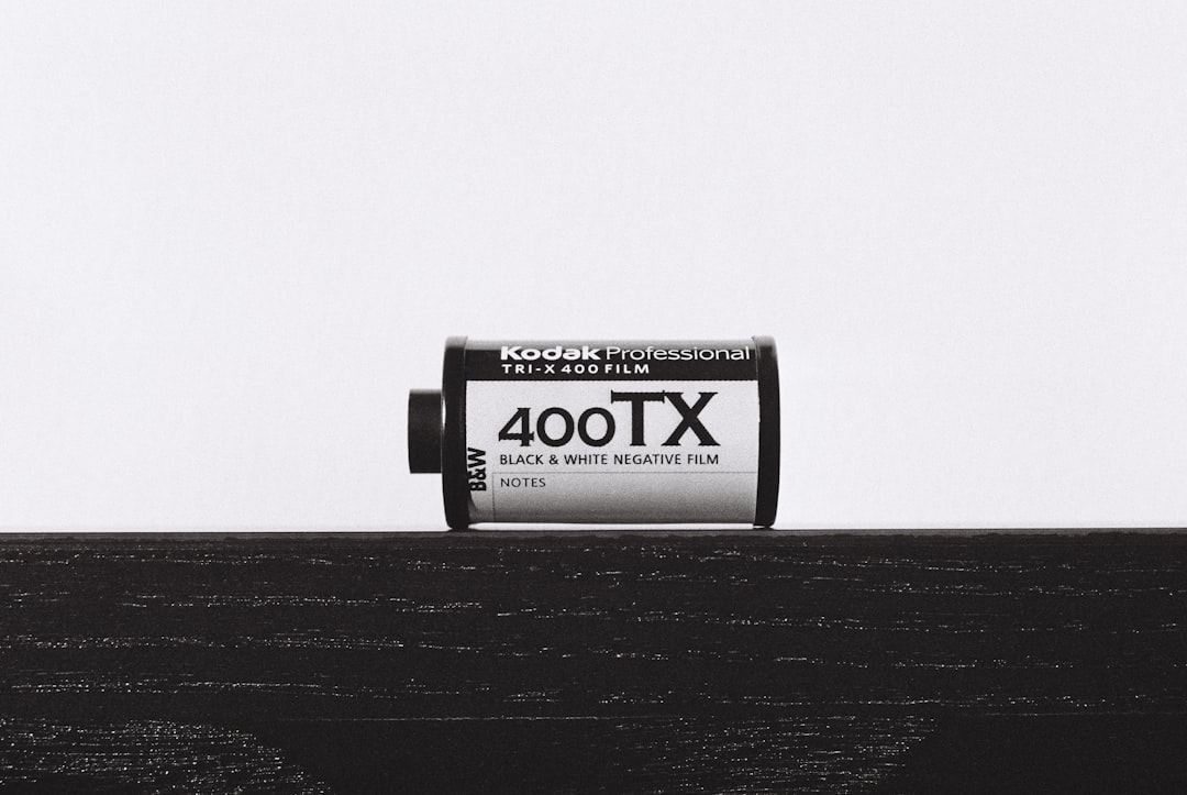 A black and white film roll with the words “Kodak Professional”, “400TOX” written on it, sitting atop an isolated dark wooden table against a stark white background. The film reel is centered in frame, its label clearly visible from behind. This minimalist composition captures the essence of classic photography aesthetics, emphasizing simplicity and clarity in visual representation. –ar 128:85