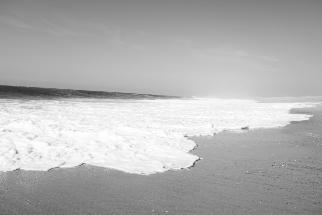 Black and white photograph of the beach with waves, surf in the distance, white foam on sand, high contrast, minimalist style, neutral tones, wideangle lens, natural light, calm sea, and a peaceful atmosphere. –ar 128:85