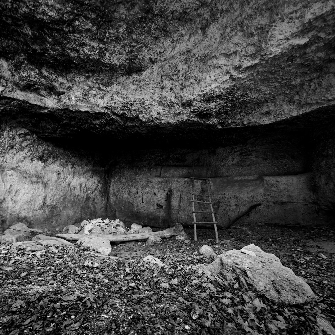 Black and white photography of an ancient cave with some old wooden ladders, rocks, wood chips on the ground, mysterious atmosphere, captured by Sony Alpha A7 III