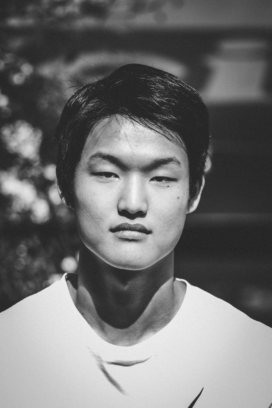 A black and white portrait of an Asian male college student, wearing sports  with short hair. The background is blurry, in the style of film grain effect, with soft edges and atmospheric effects, delicate texture, light tones, large aperture, natural environment, frontal composition, in focus. –ar 85:128