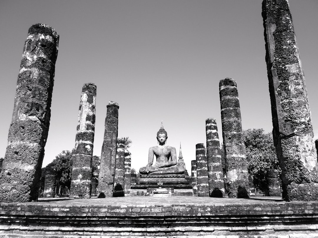 Black and white photography of an ancient temple with broken pillars, the main focus is on a sitting Buddha statue in front of it. The scene captures the grandeur of the old architecture against clear skies. –ar 4:3