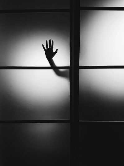 A hand is seen through frosted glass, creating an eerie silhouette against the stark black and white background. The focus on shadows adds to its mysterious ambiance. The black background and simple, minimalist style contribute to the overall effect. --ar 3:4