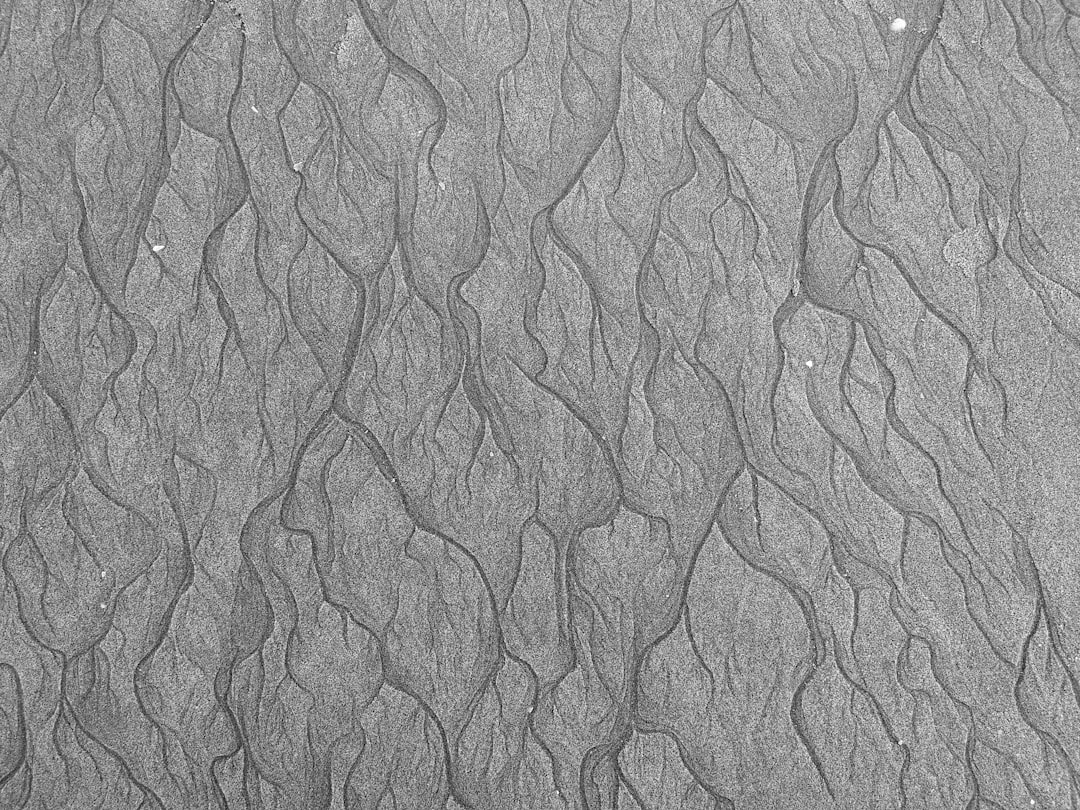 A high-resolution, detailed texture of sand ripples in black and white. The intricate pattern has visible lines on the surface, resembling fine patterns found at coastal beaches or shorelines. It is suitable for use as an abstract background or wallpaper design, offering a unique visual experience to any project that gives off natural elements. This textured background adds depth and realism while maintaining simplicity. –ar 4:3