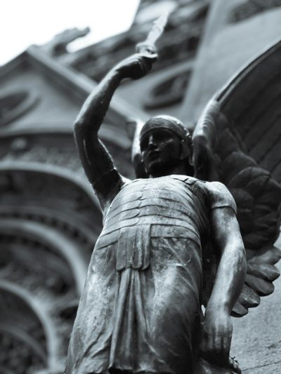 A photo of an angel statue holding up the hand in front, standing on top of parisian building. The background is the cathedral with arches and columns. In black and white. The style should be a closeup, high resolution, detailed photography. High contrast, sharp focus, shot from below. The atmosphere is somber, sad, and melancholic. There's a sense that time has stood still at this place. --ar 3:4