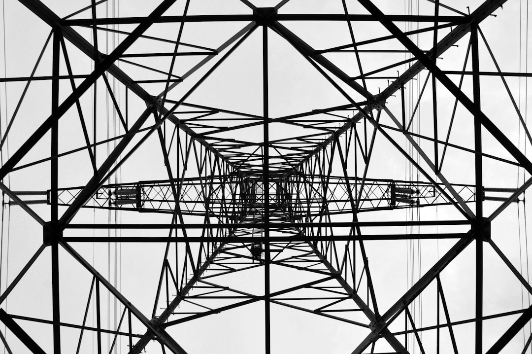 electricity provides nuanced photography in black and white. It features a close up of a power tower with a geometric and symmetrical composition. –ar 128:85