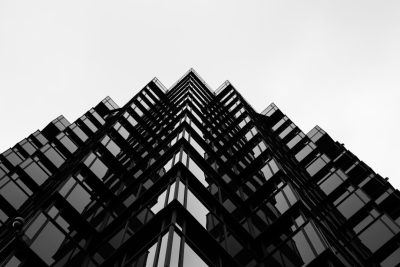 A black and white photo of the corner top floors of an office building with glass windows, symmetrical, looking up from ground level, high contrast, sharp focus on edges of window frames, minimalist style, urban architecture photography, shot in the style of Sony Alpha A7 III camera. --ar 128:85