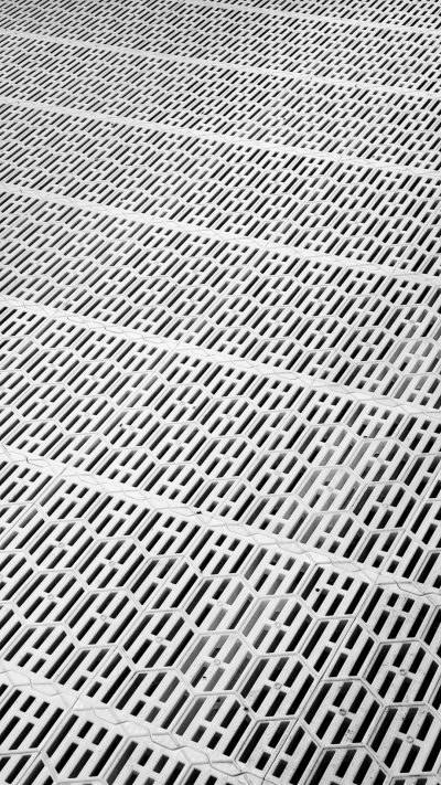 High resolution photograph of a close up view of the metal grating on an outdoor floor, emphasizing its texture and pattern in monochrome tones. The grates create intricate patterns with their slats and designs, adding depth to the composition. This perspective highlights how these architectural elements can bring life into industrial spaces or open air areas. --ar 9:16