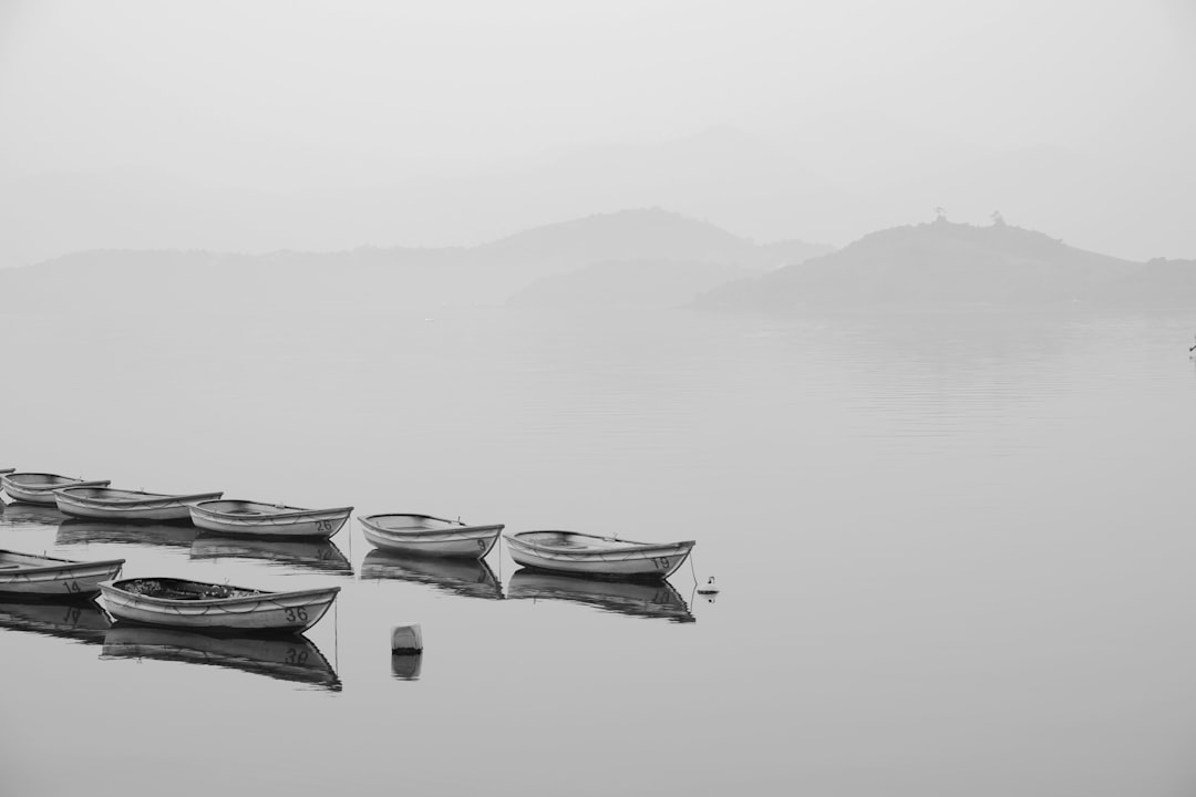 Black and white photography of boats on the lake, landscape with mountains in the background in a minimalist style, foggy weather scene, minimalist works of art, –ar 128:85