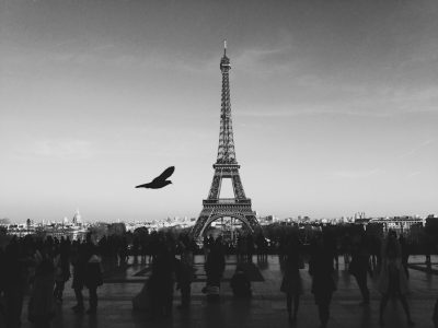 a black and white photo of the eiffel tower with people walking around, one bird flying in front of it, unsplash photography style, --ar 4:3