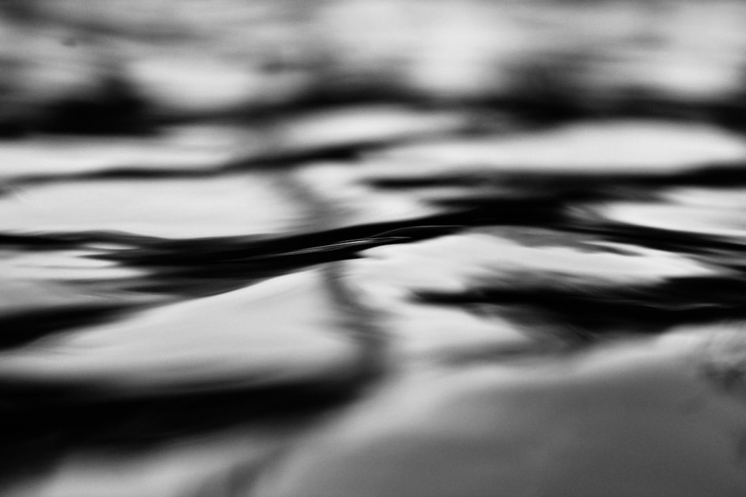 black and white abstract photograph of water ripples, blurry, grainy, high contrast texture on a black background, macro photography with motion blur, monochrome depth of field, low light and shadow play, highly detailed in the style of hyperrealistic, shot with a Leica M6 using Fujifilm Neopan Acros film stock –ar 128:85