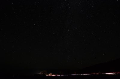 Starry sky, clear night, stars twinkling in the blackness of space, distant lights from ships or cars on one side of frame, creating long shadows across landscape, shot with Nikon D850 and Fujifilm Provia film --ar 32:21