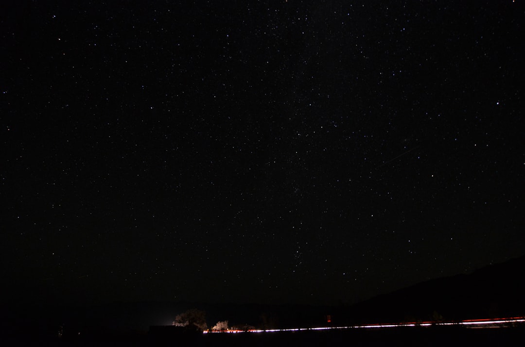 Starry sky, clear night, stars twinkling in the blackness of space, distant lights from ships or cars on one side of frame, creating long shadows across landscape, shot with Nikon D850 and Fujifilm Provia film –ar 32:21