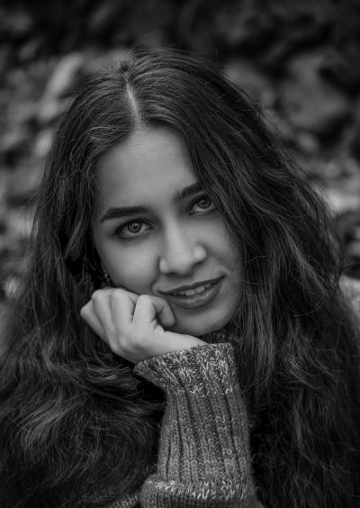 Portrait of an indian woman, smiling with hand on chin, wearing sweater and long hair, looking at camera, black & white, in forest, portrait photography, Canon EOS R5 --ar 45:64