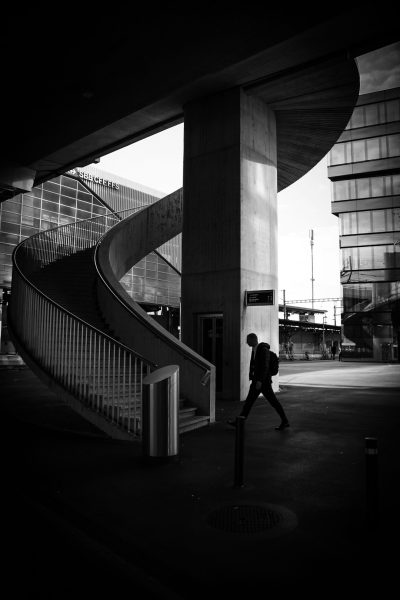 Black and white photography of an urban scene in London, a man walking under the curved staircase at Theund Wolf station in the style of Lurie. --ar 85:128