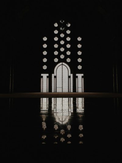 A black background with the reflection of an Islamic mosque door in a symmetrical composition with minimalism and dark tones in the style of a minimalist. A large window is at its center that reflects the light from above. The overall atmosphere is mysterious and elegant. --ar 3:4