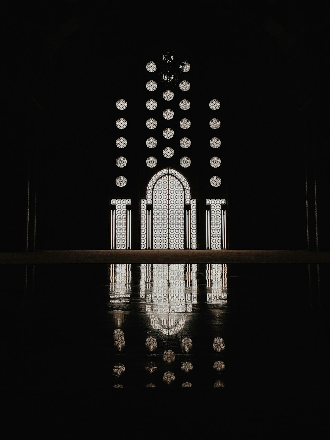 A black background with the reflection of an Islamic mosque door in a symmetrical composition with minimalism and dark tones in the style of a minimalist. A large window is at its center that reflects the light from above. The overall atmosphere is mysterious and elegant. –ar 3:4