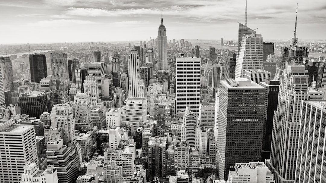 A black and white photo of the New York City skyline, showcasing its towering skyscrapers, bustling streets filled with people, cars, and buses, capturing the essence of urban life in one frame. The cityscape is filled with iconic buildings like the Empire State Building, Art Deco style architecture, and modern high-rise towers. Shot from an aerial perspective overlooking Manhattan to show the vastness of the metropolis in the style of a photo. –ar 16:9