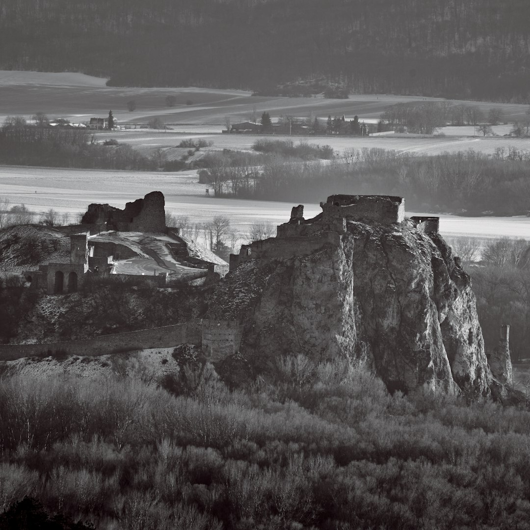 Black and white photograph of the ruins of an ancient castle on top of hill overlooking a valley with medieval villages, late winter, early spring morning, shot from high above