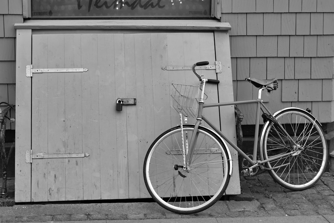 Black and white photograph of an old bike leaning against the door to a restaurant in Nantucket, with large wooden panels on it, taken from about eye level. The bicycle is a gray metal frame with small black handlebars in the style of rococo style. –ar 128:85