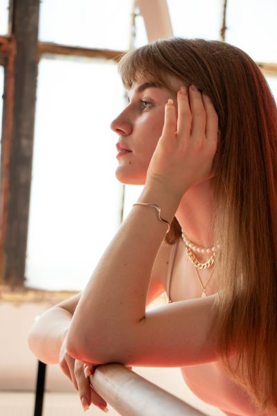 Photo of an attractive Russian girl with long straight hair, wearing pearl earrings and silver bracelet, resting her head on the handrest in front of a ballet barre, sunlight through a window behind, shot in the style of Canon EOS R5 at F2 ISO40. --ar 85:128