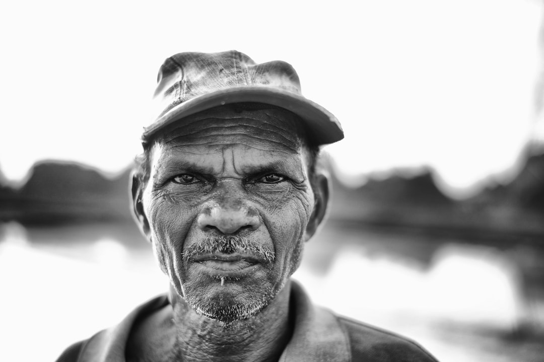 Black and white portrait of an African fisherman in front of the river, showing his face with focus on emotions against a white background, captured in the style of Sony Alpha A7 III camera using black & white film. –ar 128:85