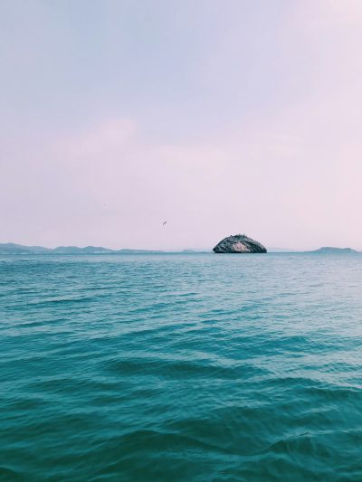 The vast sea, with an island in the distance and sky blue water. The calm light green ocean is in front of you, with some islands floating on it. There is no one around. Minimalism, Long Shot, Nikon photography style D850, 3D rendering, in the style of Nikon photography. --ar 3:4