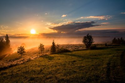 Beautiful sunrise over the misty valley, with trees and grass in the foreground, in front of it there is an open meadow. The sun rises from behind clouds. In some places you can see fog. Shot taken in the style of Sony Alpha A7 IV camera using 50mm f/2 lens at F3.4 aperture setting. --ar 128:85