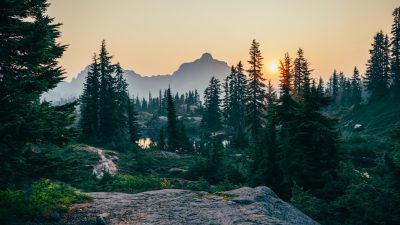 A photo of the mountain range in Washington, USA with pine trees and sunset, captured in the style of Sony Alpha A7 III camera with an f/2 lens at a focal length of 35mm, capturing the natural beauty of nature. The image showcases the rugged terrain and dense forest, creating a serene atmosphere. In sharp focus, there is a small lake surrounded by tall pines. Soft sunlight bathes the scene, casting long shadows over the landscape. This picturesque view captures the essence of wilderness. --ar 16:9