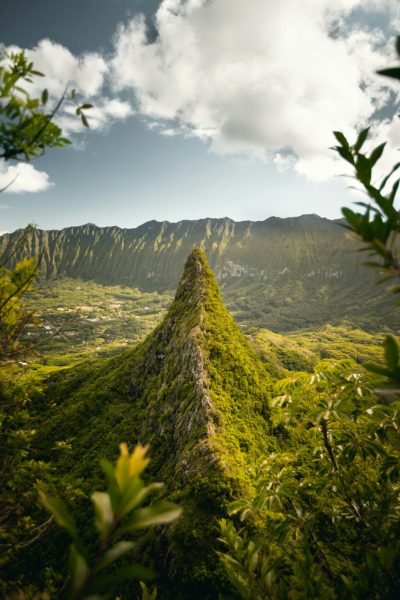 A photo of the lush green peak, Le Greges Mountain in Hawaii's volcanic très shaped mountain range. Shot with a Sony Alpha A7 III and an f/2 lens. The view is from atop le GFX showcasing its sharpness against distant mountains. Soft sunlight bathed it in golden hues. Taken in the style of photographer K birthday cake. High resolution, hyper realistic, super detailed, natural lighting, high detail, high quality. --ar 85:128