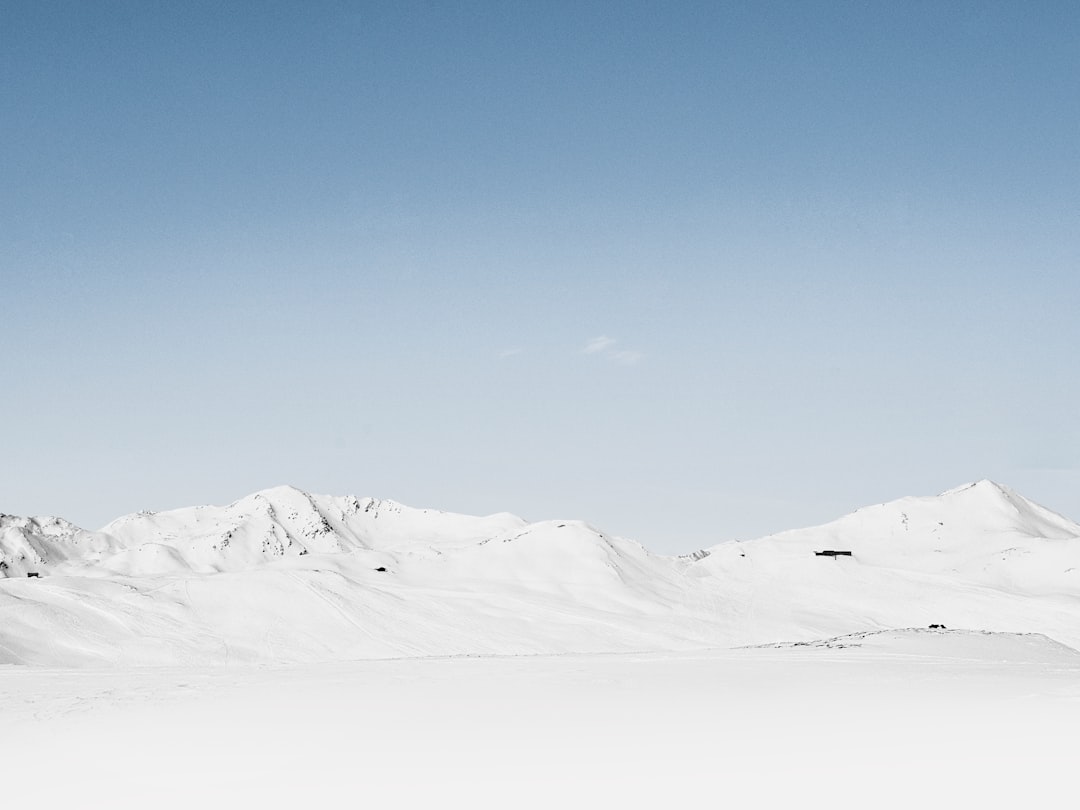 Minimalist photograph of snow-covered mountains with a clear sky and large blank space. Small people are depicted in the distance with a distant composition captured using a wide-angle lens. Cool tones and soft lighting create a static image with pure white and blue colors. The photography style has high definition and ultra-high resolution, resembling the style of high definition photography. –ar 4:3