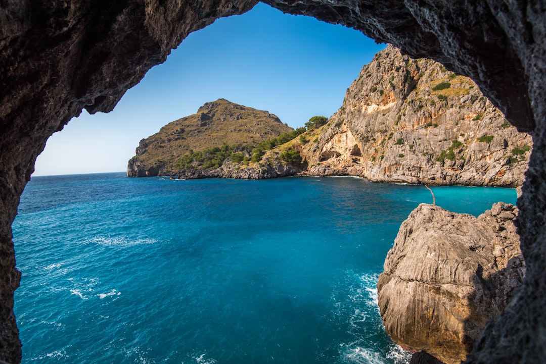 photograph of a mysterious cave on the island of Mallorca with a blue sea and green mountain, view from inside to outside, blue sky, sunny day, in the style of national geographic photography –ar 128:85