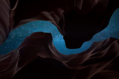 A starry night sky seen from inside an ancient canyon, with dark rocks and vibrant blue stardust, creates a surreal contrast against the black background. The composition focuses on the interplay between light and shadow in nature's symphony under the celestial canvas. In the style of Nikon D850 photo. --ar 128:85