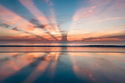 Beautiful sunset over the ocean with reflections on sand, flat horizon line, sky and clouds, mirror effect, tranquil beach scene, wide angle, telephoto lens, high resolution camera, landscape photography, award winning photo, National Geographic magazine quality, HDR photography, soft natural light, sunset colors, calm sea water, blue purple orange pink hues, reflection of colorful sky in wet sand. The sky is reflected in the shallow waves on the shore. A dreamy evening atmosphere. --ar 128:85