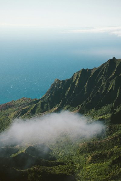 a photo of the green mountains in Kauai, with fog rolling over them and ocean view in distance, unsplash photography style, --ar 85:128