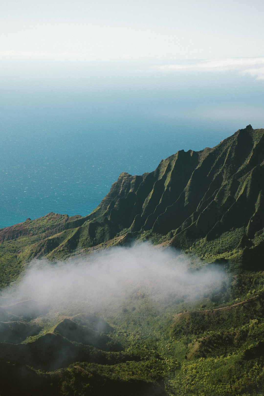 a photo of the green mountains in Kauai, with fog rolling over them and ocean view in distance, unsplash photography style, –ar 85:128