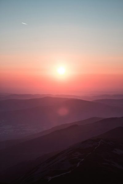 Sunset, distant mountains, light pink sky, red sun in the middle of two hills, shooting from high altitude, photography style, real details, high definition images, high resolution. --ar 85:128