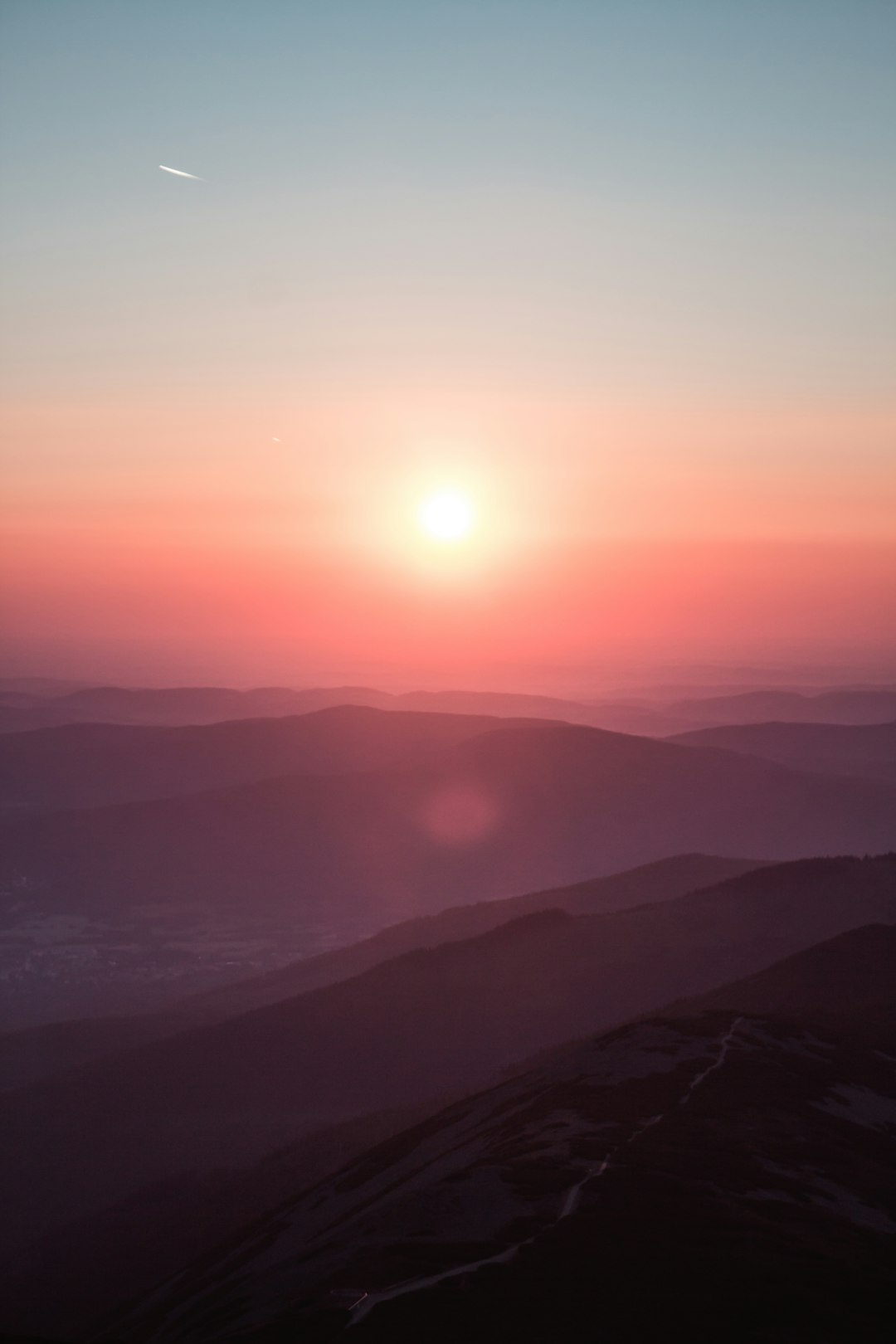 Sunset, distant mountains, light pink sky, red sun in the middle of two hills, shooting from high altitude, photography style, real details, high definition images, high resolution. –ar 85:128